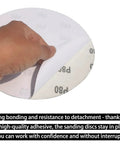Hand peeling back an 8-inch self-adhesive 80 grit sandpaper disc from 30 Pack 8 Inch Self Adhesive Sanding Discs Set Grit 80 100 120 180 240 400 For Drywall Floors Woodworking And Metal Projects Sticky Back Sandpaper Discs Great For Paint Prep Rust Busting Deburring And Smoothing