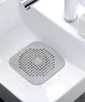 A Total Game Changer 3 Pack Silicone Drain Catchers For Sink And Tub Reusable Hair Strainers in clear silicone with hair in sink.