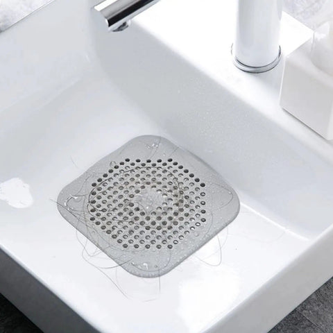 A Total Game Changer 3 Pack Silicone Drain Catchers For Sink And Tub Reusable Hair Strainers in clear silicone with hair in sink.