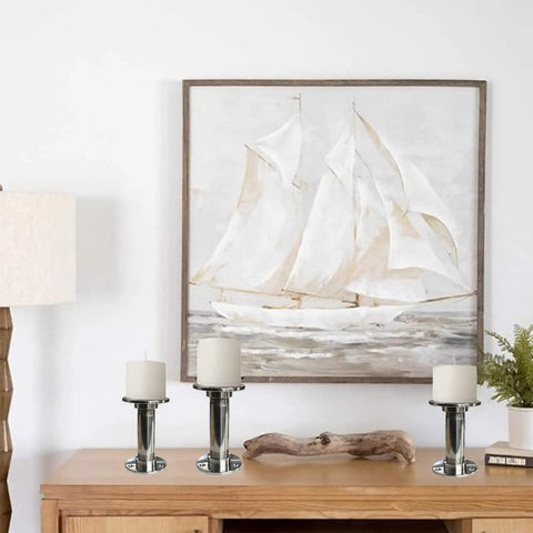 Three stainless steel candle holders on a wooden table with nautical painting in the background, modern home decor on display