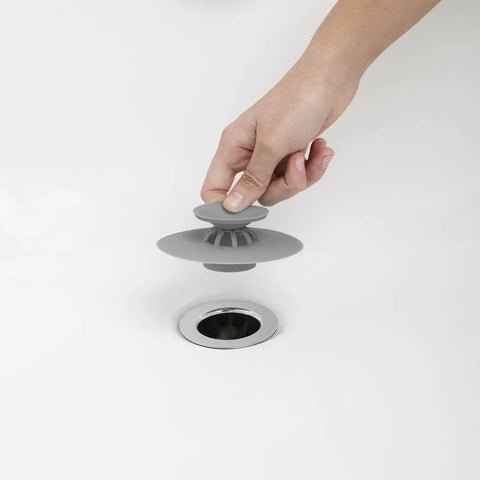 Hand placing Dual Purpose Silicone Shower Drain Stopper And Hair Catcher grey silicone over drain in bathtub.
