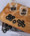 Black Eyeglass Frame Grips Hinge Tighteners Pack Of 10 displayed on wooden tray in clear containers