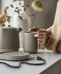 Person using a ceramic tea set on a counter with an extension cord nearby in a home setting