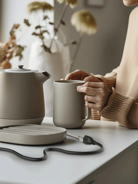 Person using a ceramic tea set on a counter with an extension cord nearby in a home setting