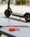 Electric Scooter Charging Port Socket With Waterproof Dust Cover for Pro Accessories Replacement Silicone Connector Red Black Durable No Fuss Easy Install Reliable Charging Port for Daily Commutes placed on table with scooter in background.