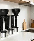 Kickass Wall Mounted Funnel Organizer Rack With Heavy Duty Iron Frame For Hella Tight Workshop Storage And Rust Resistant Industrial Shelf Brackets System, with black funnels and silver cups on a wall.