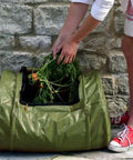 Person adding waste to Roll Mix Compost Bin Tumbler For Home Garden Green 41 Gallon Capacity 26 Inches Wide Hassle Free