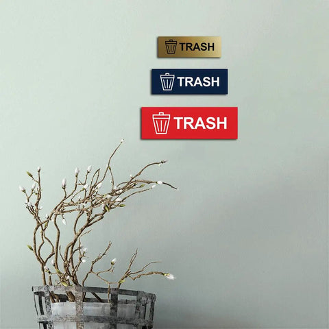 Wall display of three trash signs in different colors, including the Basic Trash Sign Brushed Silver Small For Walls Or Doors.