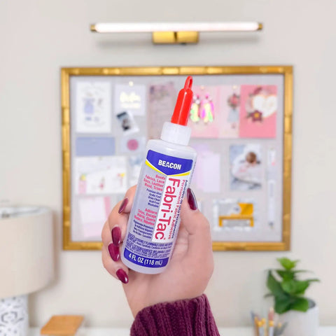 Person holding Fabri-Tac Premium Fabric Glue Quick-Drying Crystal Clear Permanent Bond For Fabrics Canvas Lace Wood And More 4-Ounce
