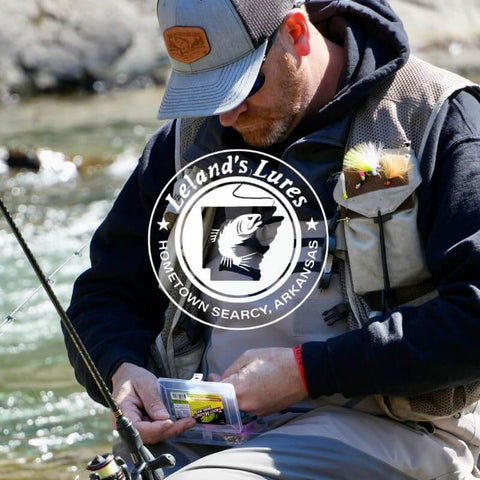 Angler using 142-Piece Trout Fishing Gear Kit With Neon Grub Lures by a river, focused on tackle box.