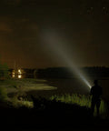 Person using Heavy Duty Handheld Spotlight With 12V DC Charger to illuminate a lakeside at night, showcasing its bright halogen bulb.