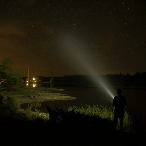 Person using Heavy Duty Handheld Spotlight With 12V DC Charger to illuminate a lakeside at night, showcasing its bright halogen bulb.