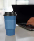 Blue 16 oz disposable paper coffee cup with lid and sleeve on desk, part of 100 pack for cafes, offices, hot and cold drinks.