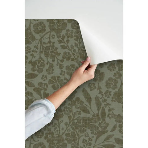 Hand peeling back Cozy Cottage Botanical Peel And Stick Wallpaper Removable Linen Texture for easy application.
