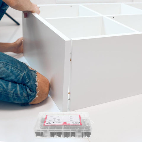 Person assembling white furniture with 141 Piece Furniture Bolts And Nuts Kit For Beds And Cribs, Aluminum Alloy Screws Set nearby.