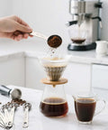Hand using Six Piece Stainless Steel Measuring Spoons Set For Cooking And Baking Includes One Eighth Teaspoon One Quarter Teaspoon One Half Teaspoon One Teaspoon One Half Tablespoon One Tablespoon Coffee Scoop Rust Resistant Food Grade Kitchen Gadgets to measure coffee over a pour-over coffee maker