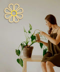 Flower Neon Sign Daisy Window Light LED Warm White For Bedroom Decor on wall, woman watering plant nearby