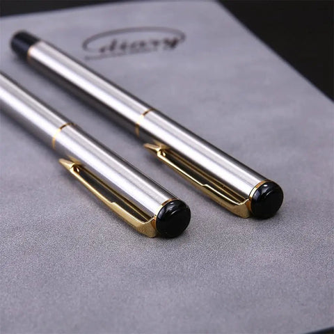 Two stainless steel golden rollerball pens on grey surface with smooth ink flow and comfortable grip, stationery essential