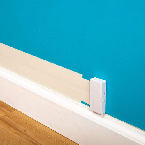 Ultra Flat Adhesive Speaker Wire 16 AWG 2 Conductor, 50 Ft White Spool, visible against a blue wall above a wooden floor