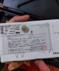 Person holding packaging for Mitutoyo product, showing specifications and a warranty card with a coin for scale