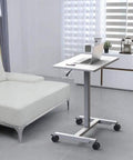Hella Sturdy Height Adjustable Mobile Standing Desk With Smooth Glide Casters And Rustproof White Steel Top Portable Laptop Workstation and Rolling Podium for Home Office Space next to a sofa.