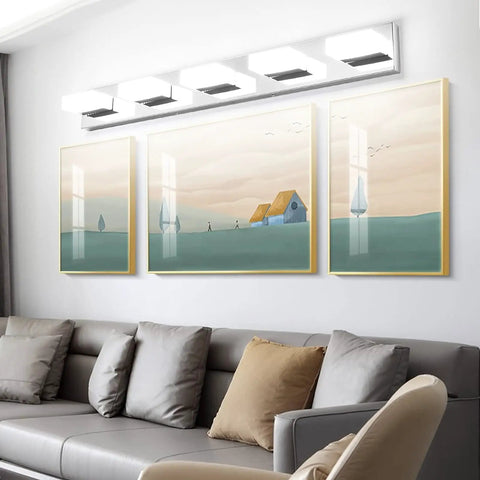 Modern Stainless Steel 3 Light LED Vanity Light Fixture With Frosted White Acrylic Shades above a sofa with art panels