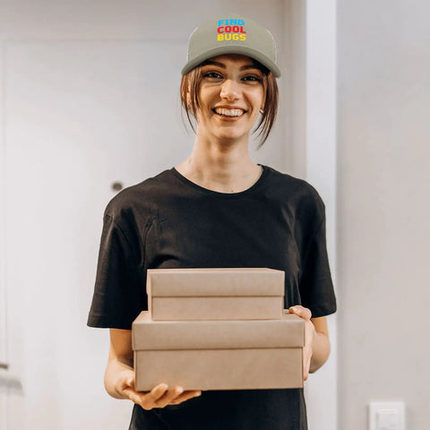 Smiling person wearing an Apricot Mesh Baseball Hat For Men And Women Cool Bugs Trucker Cap holding boxes indoors.