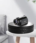 Must Have Remote Controlled 360 Rotating Turntable For Jewelry Photography And Live Streaming With Adjustable Speed Silent Motor Operation Perfect Display Stand with a camcorder on top.