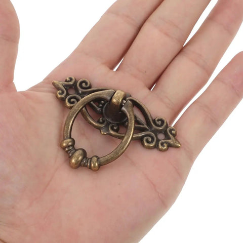 Hand holding Six Piece Vintage Bronze Bail Drawer Pulls For Dresser Cabinet Jewelry Box And Furniture Antique Round Knob Hardware Retro Vibe Durable Zinc Alloy Construction Classic Decorative Pull Handles.