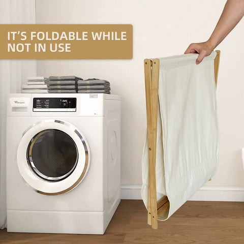 Collapsible Bamboo Wood Laundry Hamper With X Frame next to washing machine, showing foldable design for easy storage.