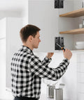 Man installing 3 Inch Black Door Hinges 12 Pack on kitchen cabinet door, showcasing 304 stainless steel construction with screwdriver.