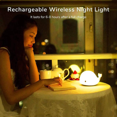 Woman reading next to Cute Whale Night Light For Kids With 7 Color Changing LEDs, Tap Control Silicone Baby Night Lamp, USB Rechargeable