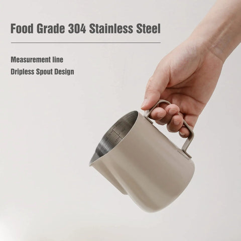 Hand holding Stainless Steel Milk Frothing Pitcher With 14oz And 20oz Capacity For Latte Art And Espresso Steam Pouring Precision Barista Grade Milk Pitcher For Cappuccino Creating Smooth Foam Durable Welded Handle showing its measurement line and dripless spout.