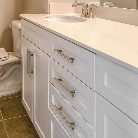 White bathroom cabinet with stainless steel T bar cabinet handles in satin brushed nickel finish installed on drawers and cupboard.