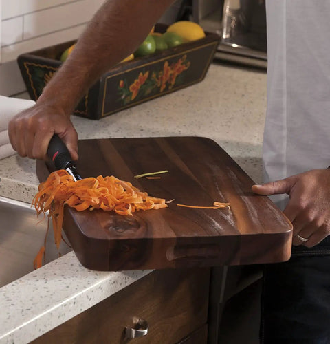 Person using a cutting board beside a sink in a kitchen setting with a bowl of fruit in the background.