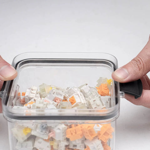 Front view of transparent plastic keyboard switch storage box filled with assorted white and orange switches.