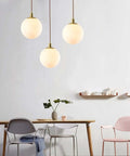 Modern Minimalist Pendant Light With White Glass Globe Shade, Premium Brass Spherical Ceiling Fixture above dining table.