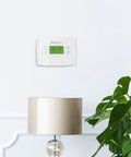 Smart 5-1-1 Day Programmable Thermostat With Early Start, One-Degree Accuracy on a living room wall above a lamp and plant