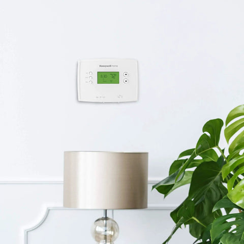 Smart 5-1-1 Day Programmable Thermostat With Early Start, One-Degree Accuracy on a living room wall above a lamp and plant