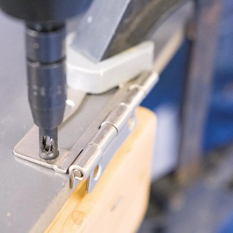 1/4 in drill bit in a drill engaged with a metal hinge plate