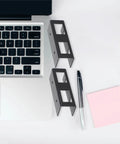 Super Tight Black Steel Laptop Stand With Storage Tray For Sick Desk Setup, displaying durable steel brackets beside a laptop.