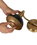 Hands assembling black and brushed gold modern farmhouse bathroom light fixture with two lights and metal shade.