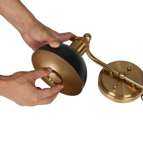 Hands assembling black and brushed gold modern farmhouse bathroom light fixture with two lights and metal shade.