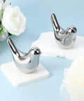 Two Ceramic Bird Toilet Bolt Covers Set in silver finish displayed on a light blue surface with white flowers in the background.