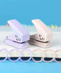 Two Pack Mini Purple And Pink One Quarter Inch Circle Hole Punch Handheld Paper And Leather Craft Tool For Punching About Ten Sheets Of Paper Durable Metal Construction Great For Scrapbooking And DIY Projects with two punches over notebook.