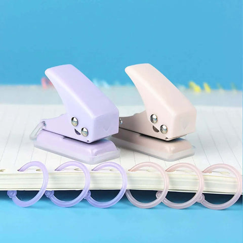 Two Pack Mini Purple And Pink One Quarter Inch Circle Hole Punch Handheld Paper And Leather Craft Tool For Punching About Ten Sheets Of Paper Durable Metal Construction Great For Scrapbooking And DIY Projects with two punches over notebook.
