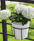 Three Pack 10 Inch Railing Planters For Balcony Or Porch Hanging Baskets Outdoor Indoor Flower Pot Holders Fits Up To Nine And A Half Inch Pots And Two And Three Quarter Inch Rail No Fuss Easy Hang Metal Fence Planters with white flowers.
