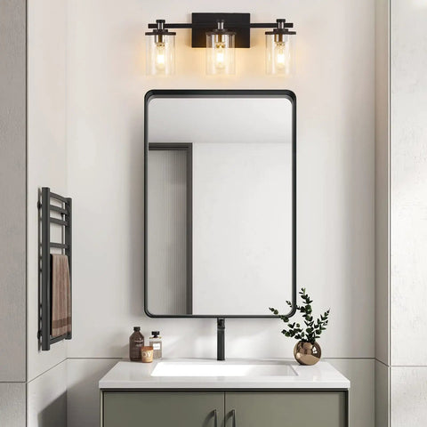 Bathroom scene with three light matte black and brushed nickel bathroom vanity light fixture over mirror, clear glass shades visible.