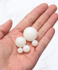 Hand holding varying sizes of PA nylon solid bearing spheres, showcasing Built Tough One Inch Nylon Solid Balls Ten Pack.