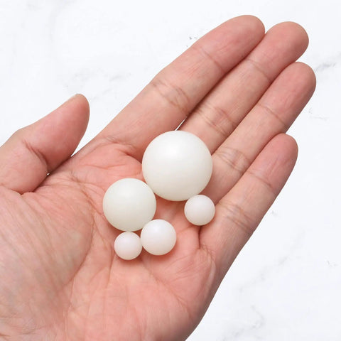 Hand holding varying sizes of PA nylon solid bearing spheres, showcasing Built Tough One Inch Nylon Solid Balls Ten Pack.